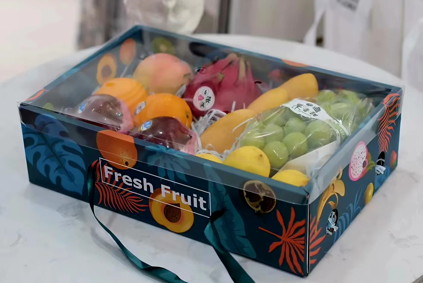 Box di frutta fresca selezionata preparato da TREVANI per le aziende: frutta esotica, uva, mele, pere, pitaya, mango — confezione regalo con coperchio trasparente